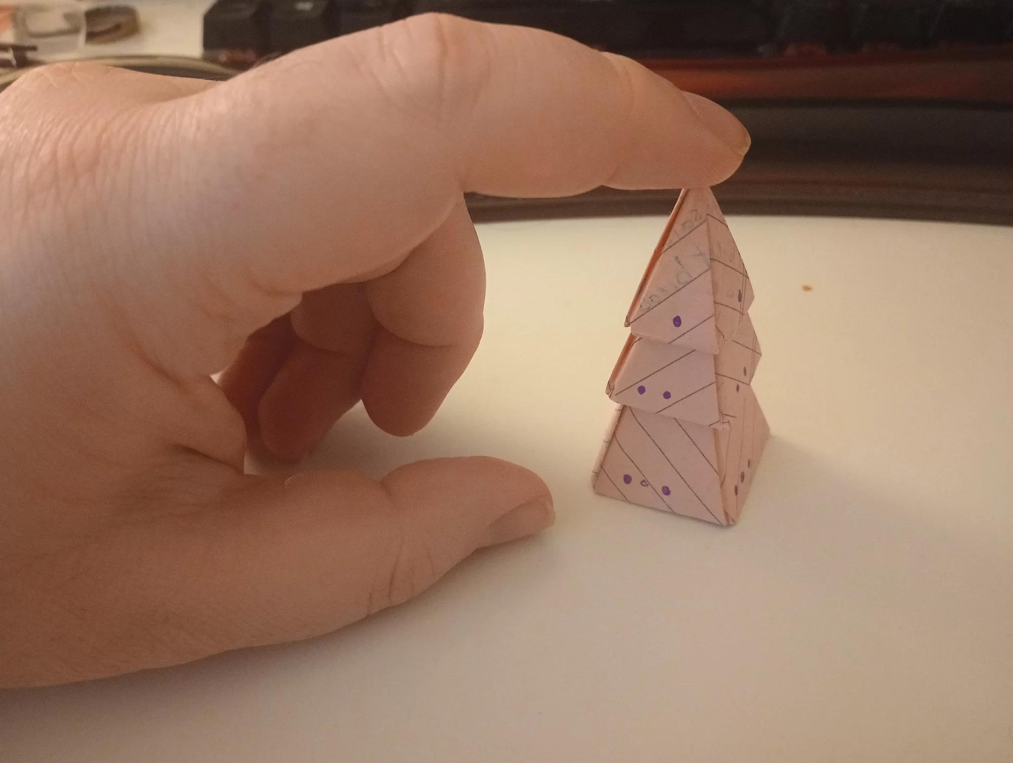 three paper pyramids stacked upright in a pine tree shape, with a hand visible holding them in place.