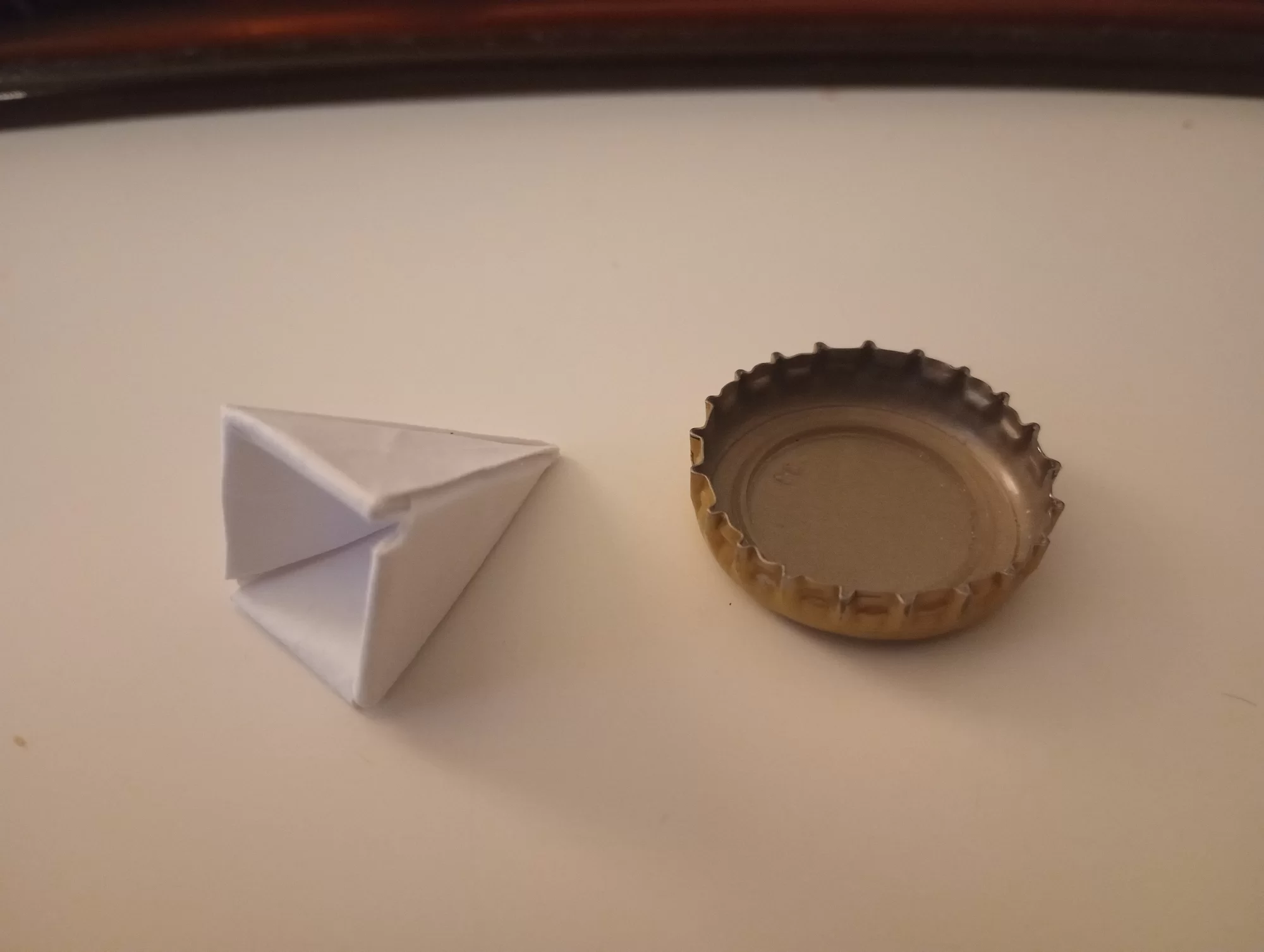 a paper pyramid next to a bottlecap, for scale. the pyramid is about half an inch wide at the base.